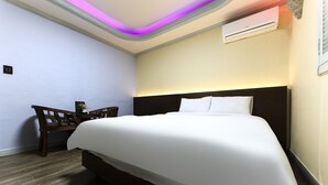 A hotel room with a bed, a desk with a chair, and a wall-mounted air conditioner.