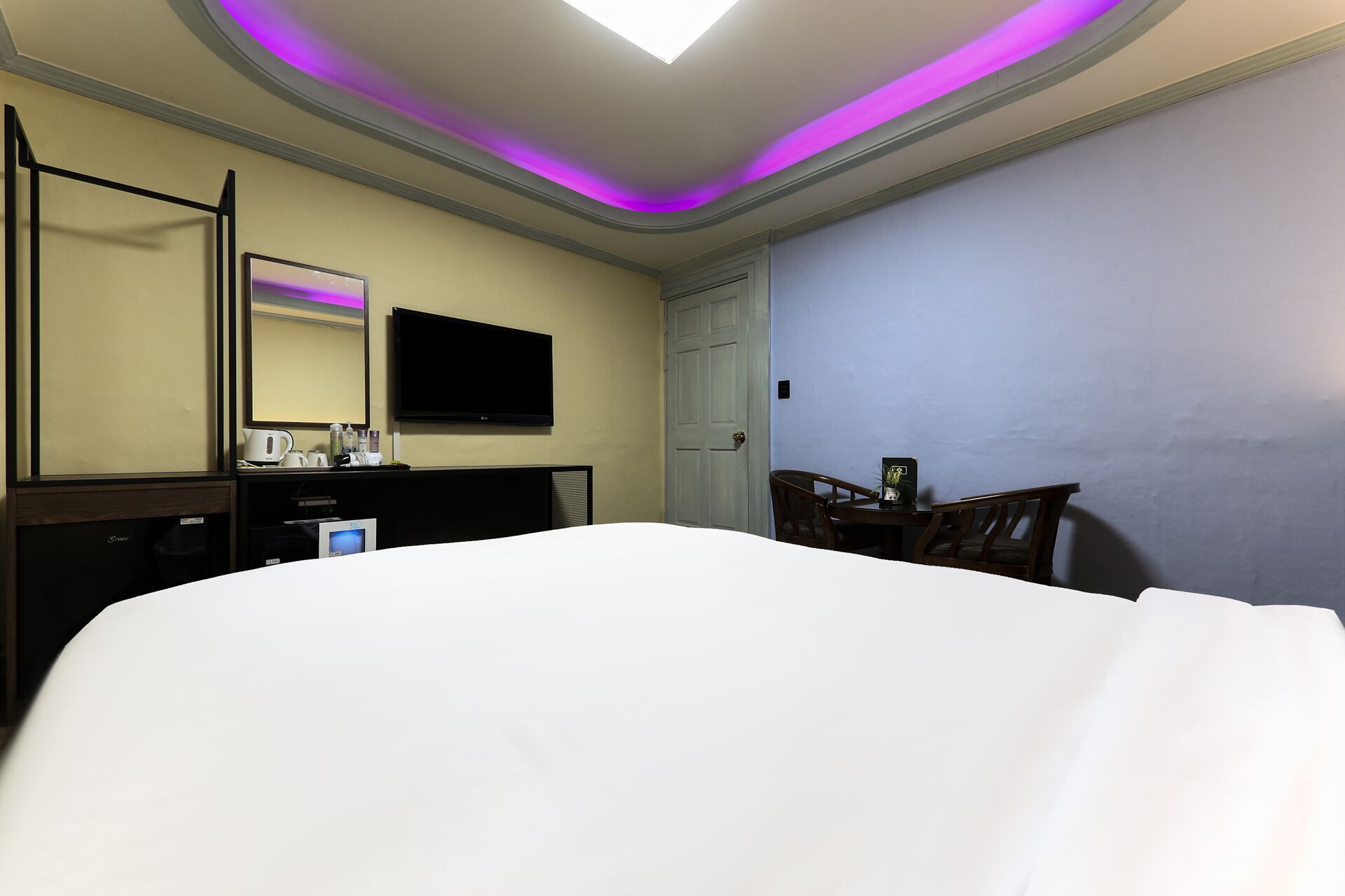 Habitación de hotel con cama, escritorio, televisor de pantalla plana, espejo y puerta.