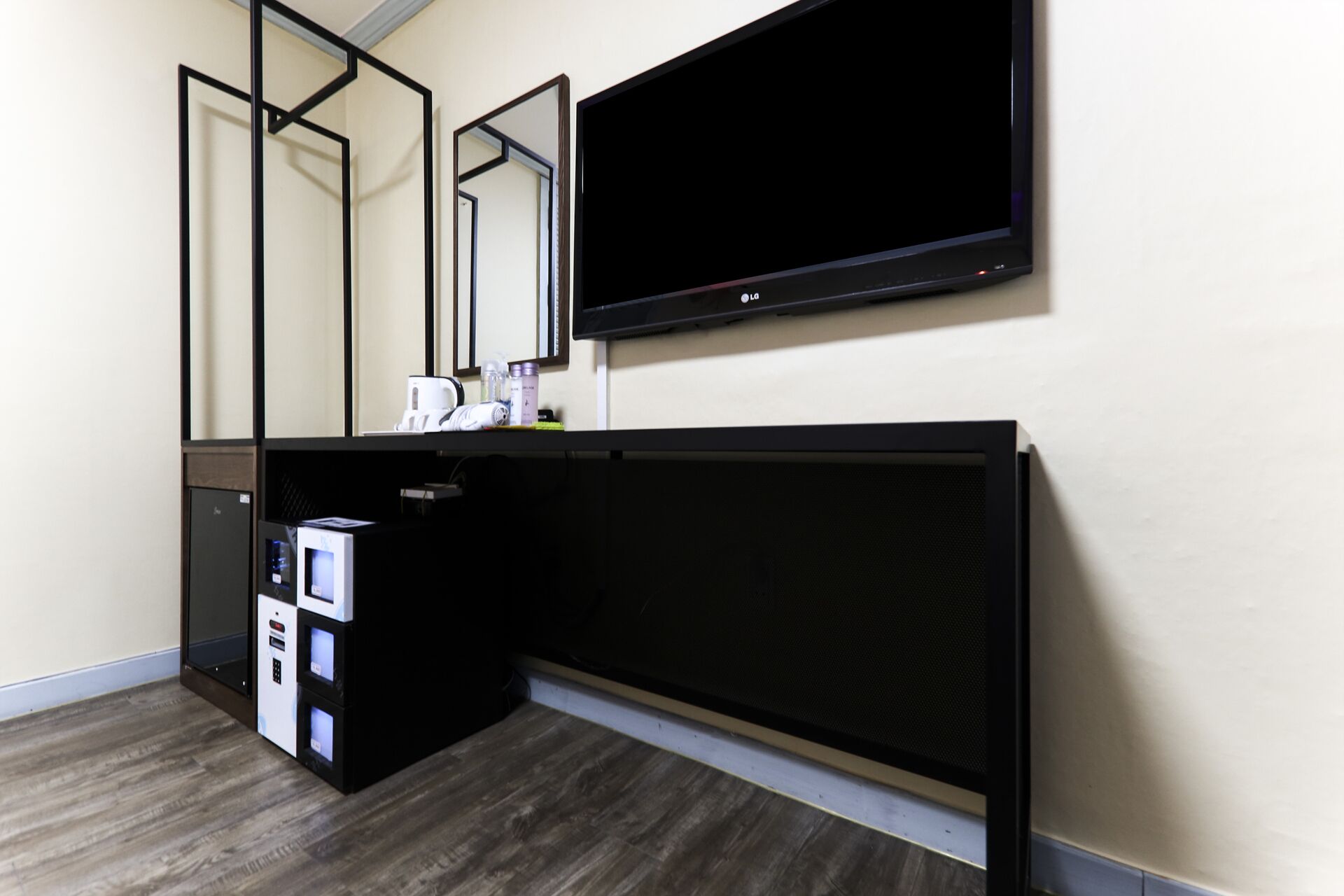 A hotel room with a black entertainment unit, a large mirror, and a flat-screen TV mounted on the wall.