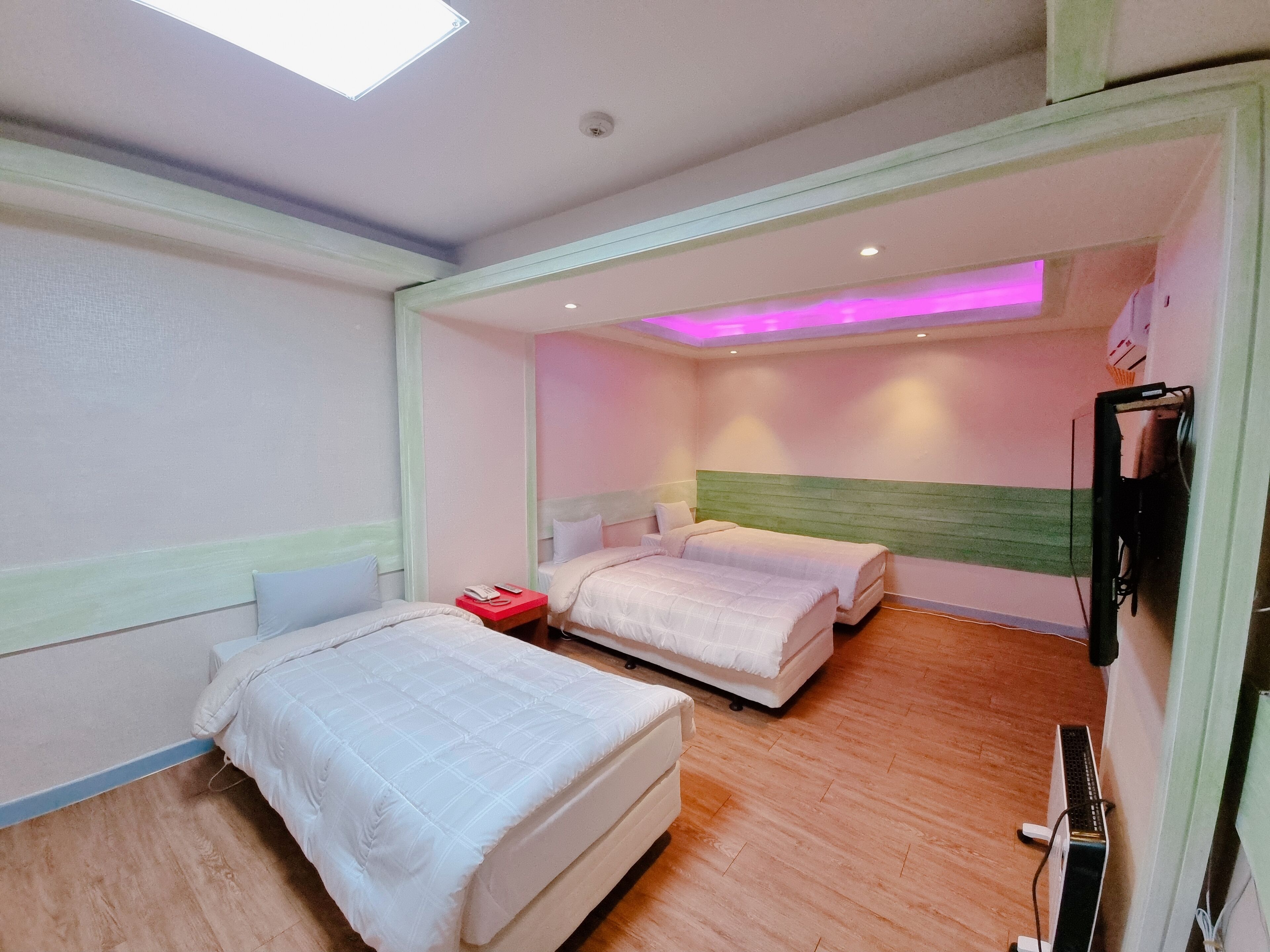 A hotel room with two beds, a desk, a chair, a flat-screen TV, and a ceiling light.