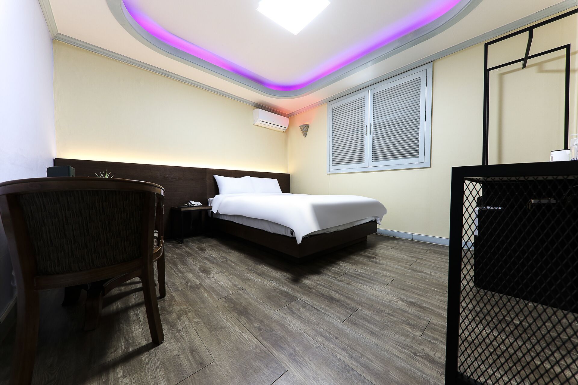 A hotel room with a bed, a desk, a chair, and a window with blinds.
