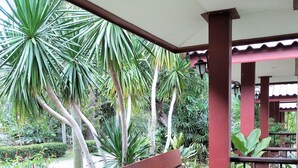 A wooden bench under a covered area with a view of tropical plants. - Phetsangsom Resort (Klaeng)