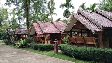 A row of wooden cabins with pitched roofs, surrounded by lush greenery and palm trees.