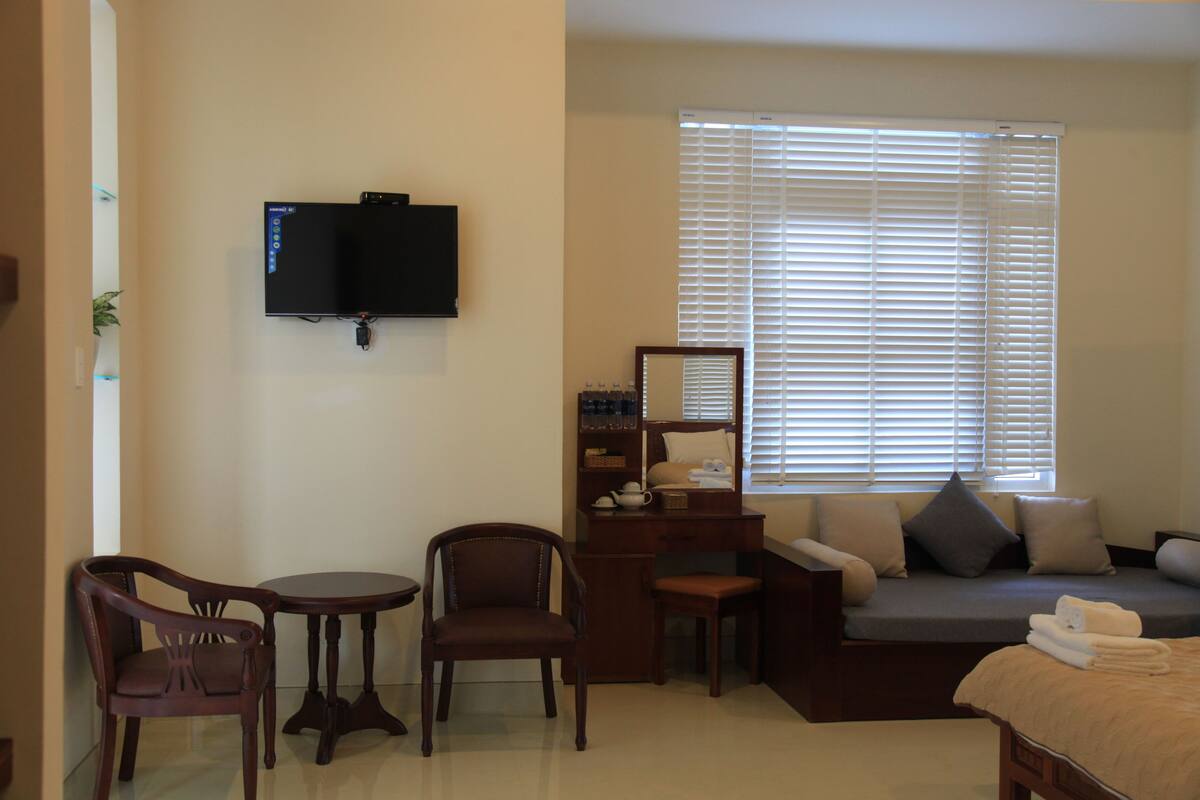 A hotel room with a bed, a desk, a chair, a TV, and a window with blinds.