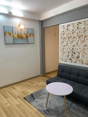 A room with a grey sofa, a round white table, a patterned rug, a wall-mounted artwork, and a decorative panel. - Oscar House (Xuan Huong - Da Lat)