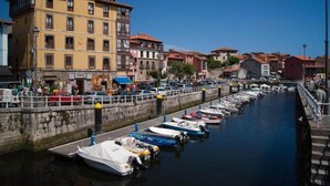 A canal with boats docked along the side, surrounded by buildings with balconies and a pedestrian walkway. - Hotel Cantábrico de Llanes (Llanes)
