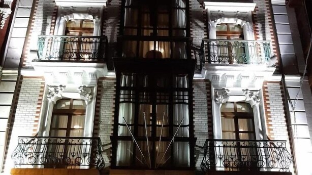 A building with a central fire escape, multiple balconies with wrought iron railings, and a ground-floor entrance with a glass door. - Hotel Cantábrico de Llanes (Llanes)