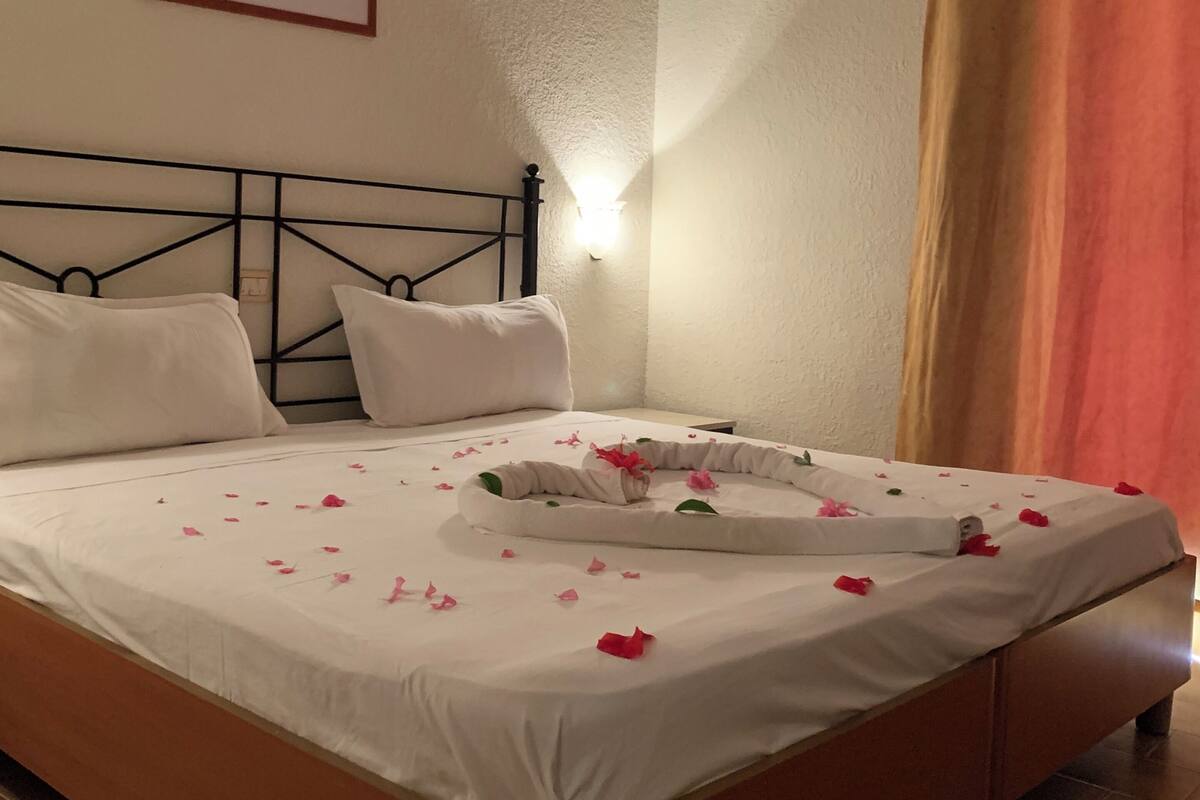 A neatly made bed with white linens and pink flower petals scattered across the surface.