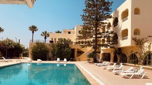 A pool area with lounge chairs and a building with multiple balconies. - Sol Palmeras Beach - Family Hotel (Sousse)