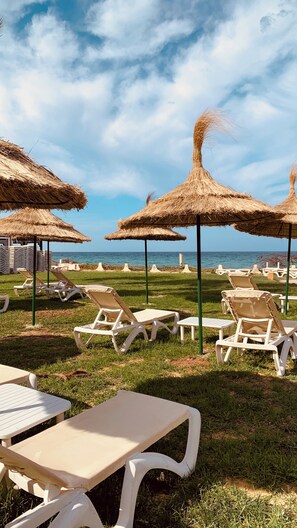 A beachside lounge area with thatched umbrellas, white lounge chairs, and a table. - Sol Palmeras Beach - Family Hotel (Sousse)