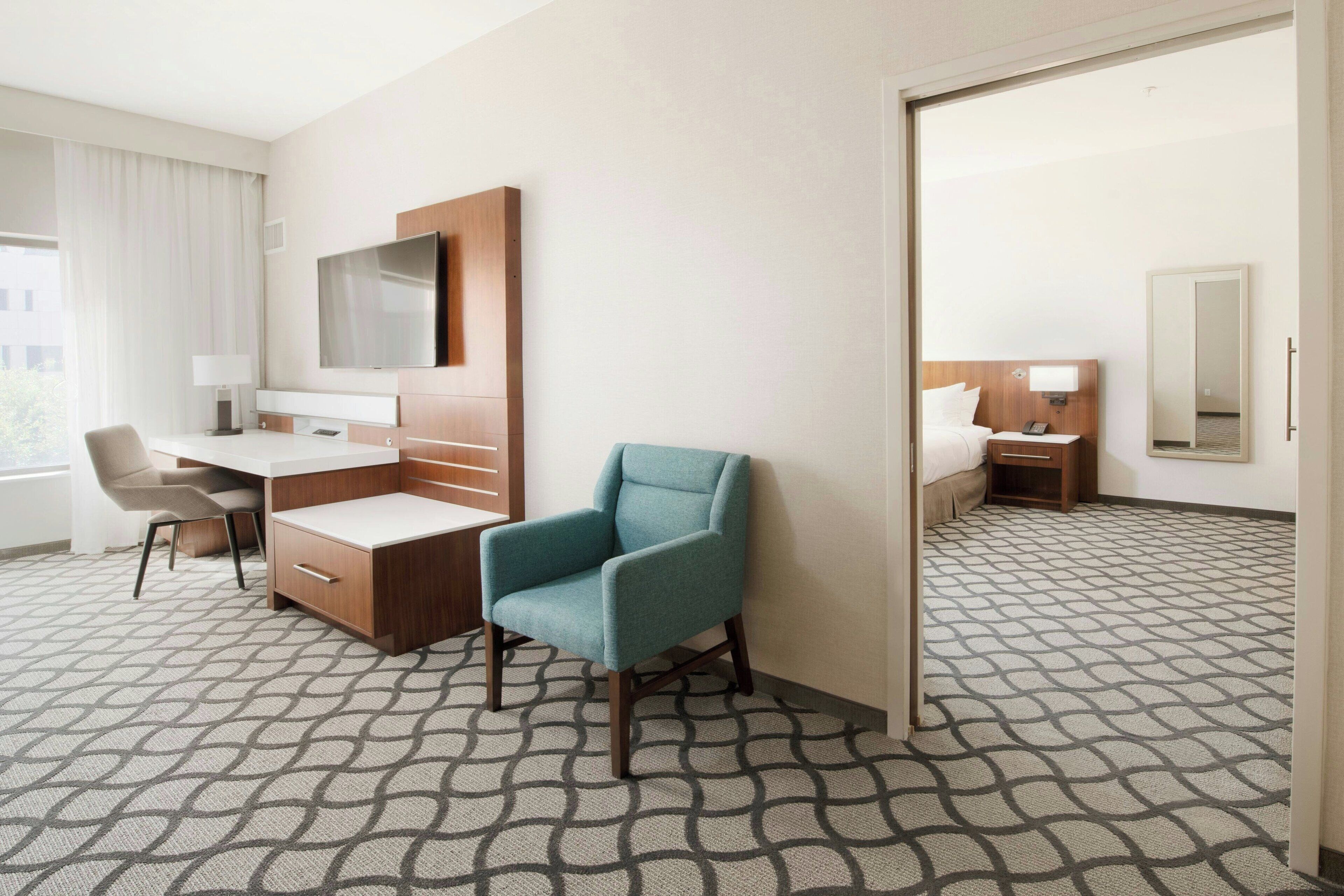 A hotel room with a desk, chair, TV, and a large mirror.
