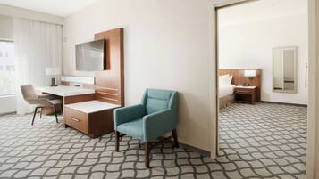 A hotel room with a desk, chair, TV, and a large mirror.