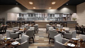 Een modern restaurant met een centrale keuken, meerdere eettafels en stoelen, geordend in een ruim opgezette indeling.
