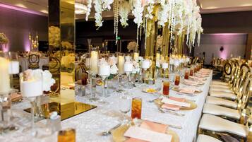 Una larga mesa de banquete con manteles blancos, platos bajos dorados y servilletas rosas.