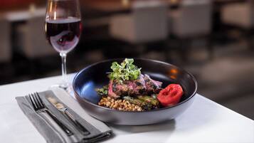 Una mesa de comedor con un plato de comida, una copa de vino tinto y cubiertos.