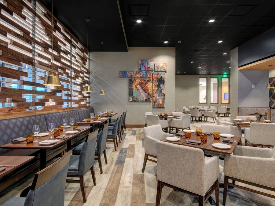 A modern restaurant with a long wooden bench seating area, multiple tables with chairs, and a large abstract painting on the wall.