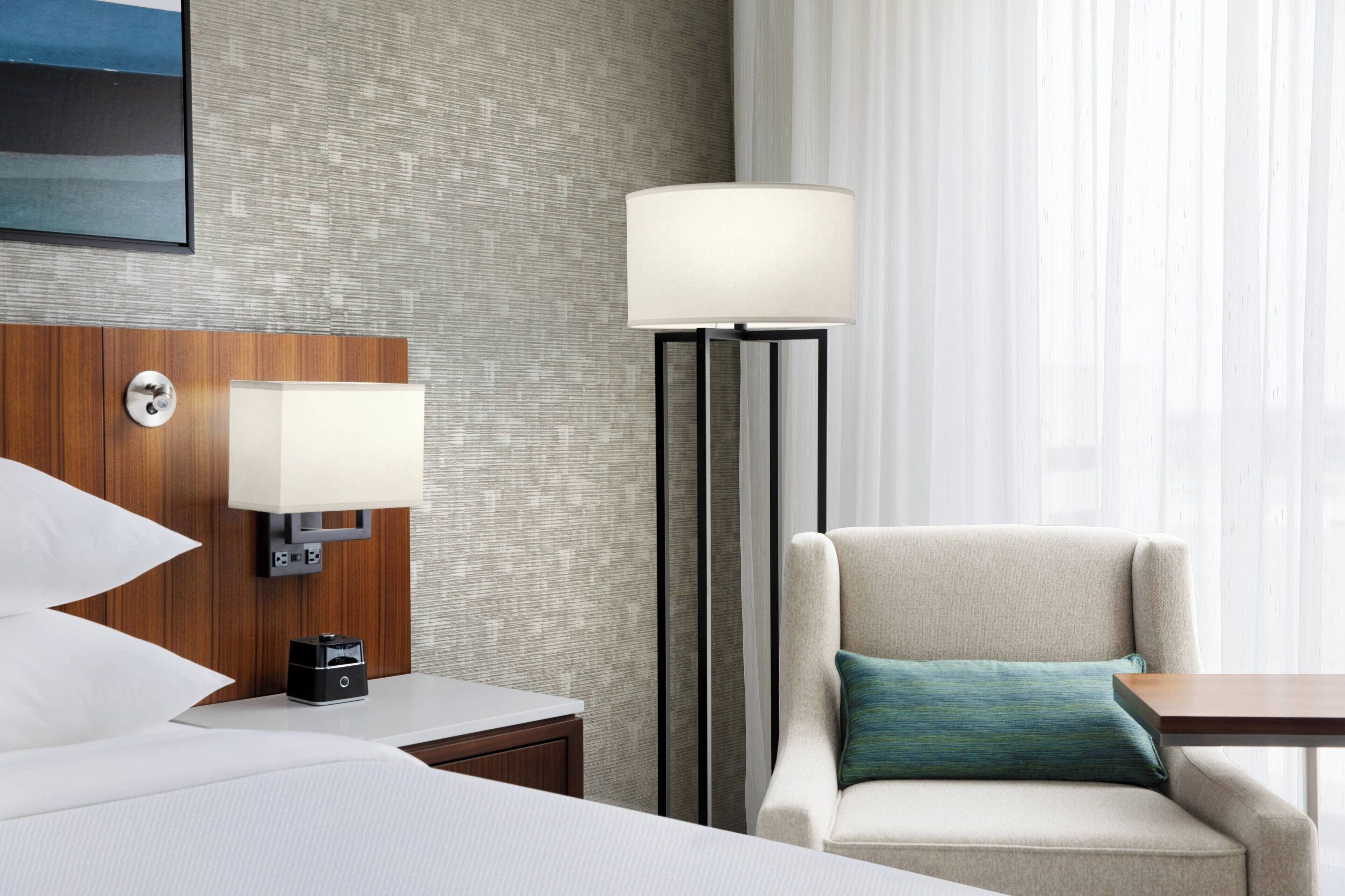 A hotel room with a bed, a nightstand, a lamp, a chair, and a table.