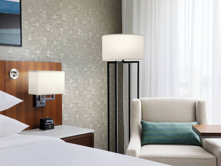 A hotel room with a bed, a nightstand, a lamp, a chair, and a table.