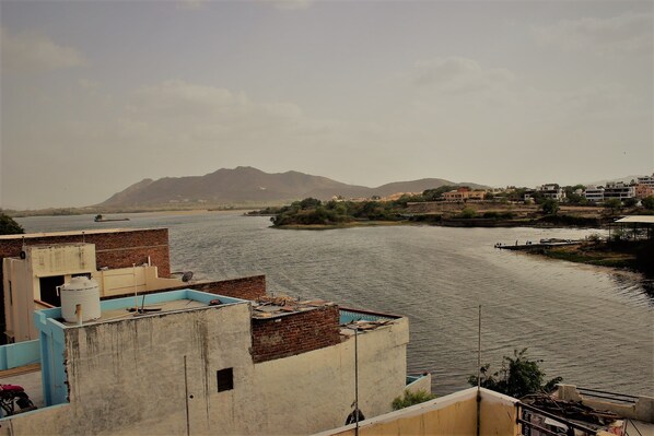A river with buildings on the banks, a distant mountain, and a clear sky. - Rising Shemesh (Udaipur)