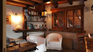 A cozy room with wooden beams, a bookshelf, two white chairs, and a window with wooden shutters. - Dormì & Disnà (Val di Zoldo)