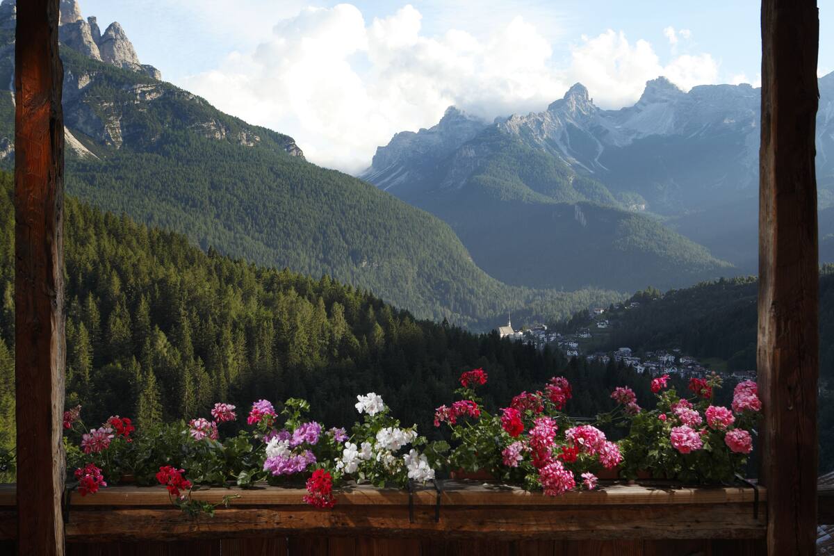 A wooden balcony with a view of a mountainous landscape and a village below.
