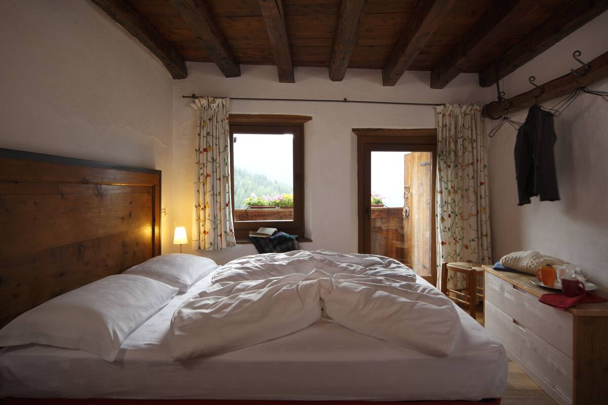 A bedroom with a wooden headboard, a bed with white bedding, a wooden dresser, and a window with curtains.