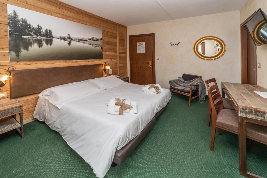 A hotel room with a large bed, a dining table, a chair, a mirror, and a painting on the wall.