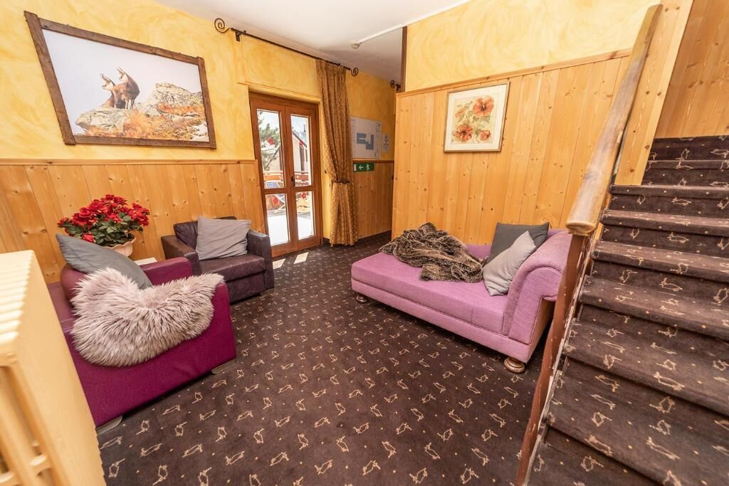 A wooden interior with a staircase, two sofas, a patterned carpet, and a door leading outside.