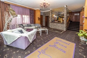 A hotel lobby with a sofa, a coffee table, a chandelier, and a stone wall. - Hotel Gran Baita (Sauze d'Oulx)
