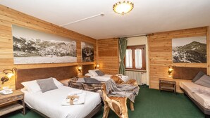 A hotel room with wooden walls, multiple beds, and large mountain landscape pictures. - Hotel Gran Baita (Sauze d'Oulx)