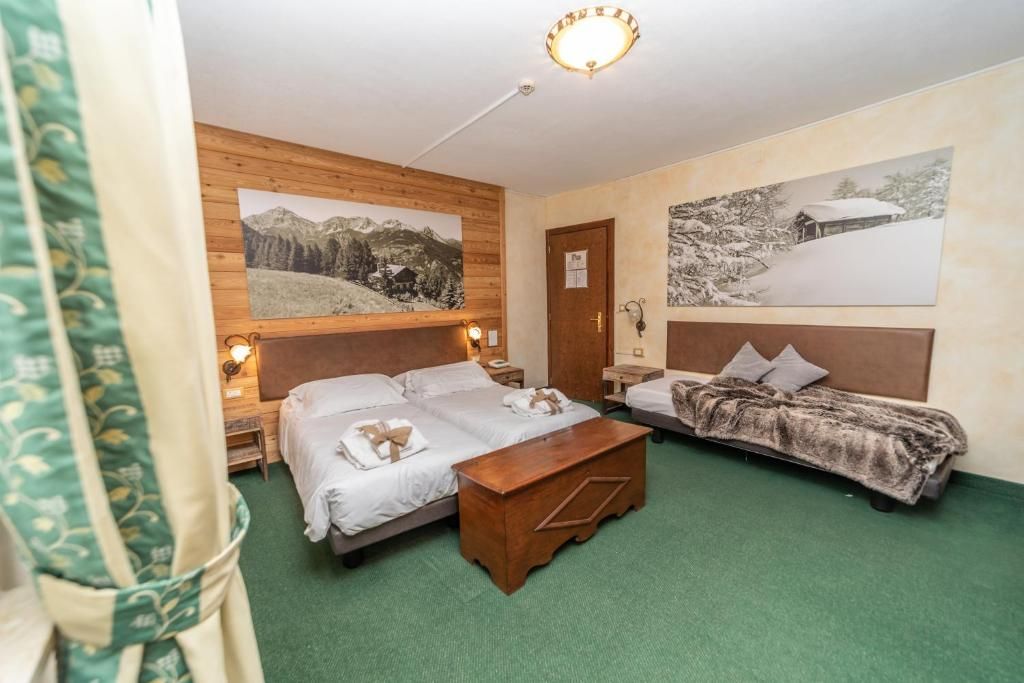 A hotel room with two beds, a wooden headboard, a green carpet, and two wall-mounted paintings.