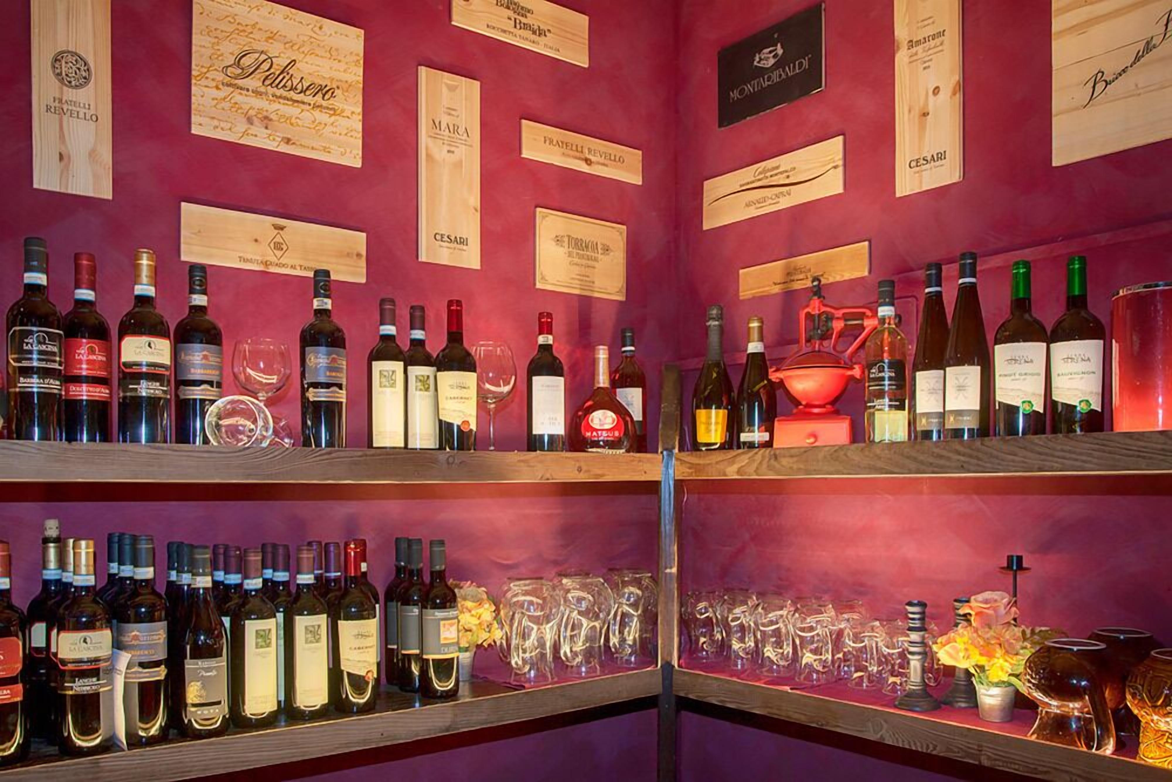 Ein Weinkeller mit Regalen voller Weinflaschen und Gläsern, Holzschildern an der Wand und einem Weinglas mit Rotwein auf der rechten Seite.
