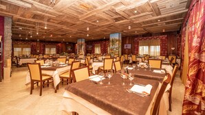 A large dining area with multiple tables and chairs, wooden ceiling beams, and large windows with curtains. - Hotel Gran Baita (Sauze d'Oulx)