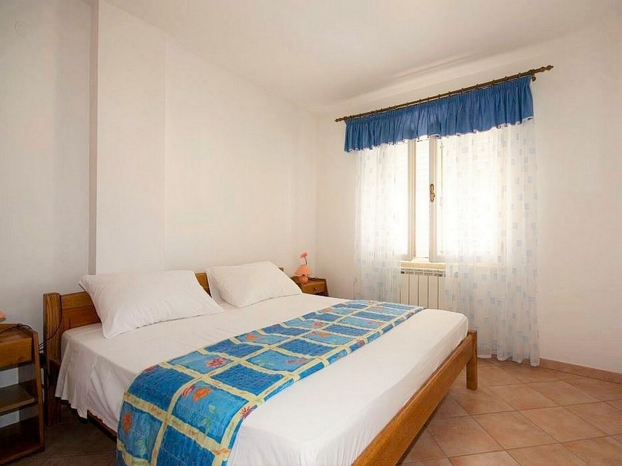 Une chambre à coucher avec un lit, une table de chevet, une fenêtre avec des rideaux et un radiateur.