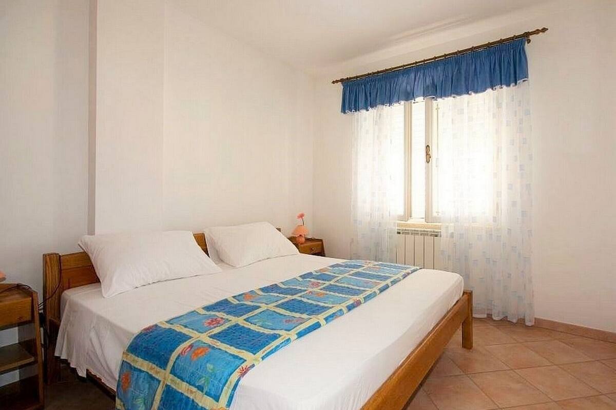 A bedroom with a bed, a nightstand, a window with curtains, and a radiator.