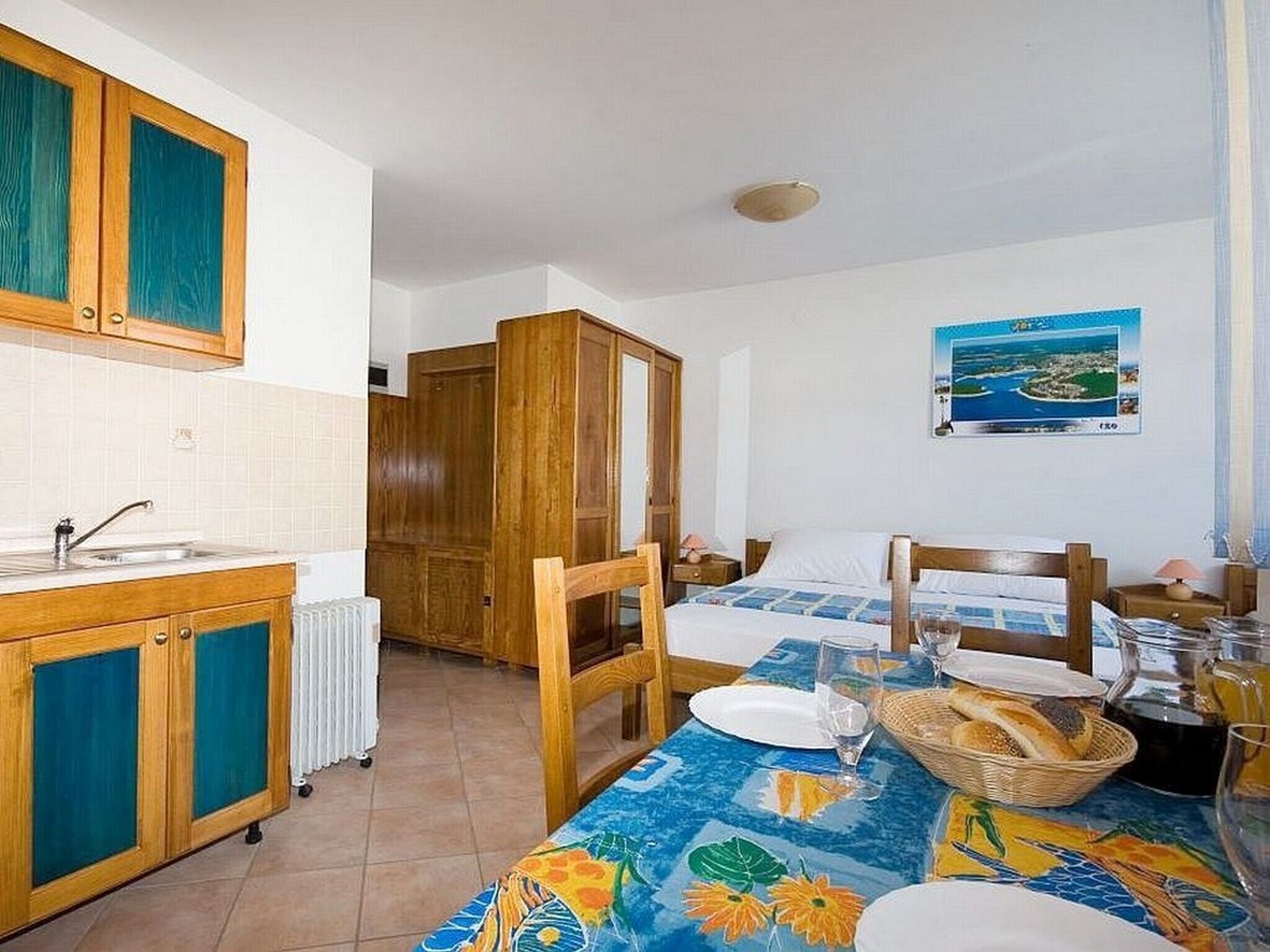 Une pièce comprenant un lit, une table à manger avec une nappe, un coin cuisine et une vue sur la mer.