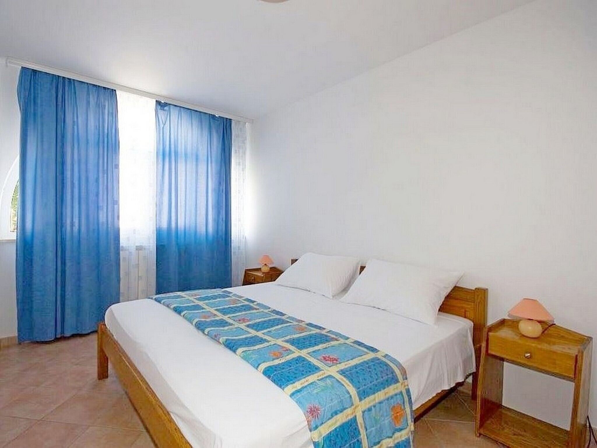 Une chambre à coucher avec un lit, des rideaux, une table de chevet et une lampe.