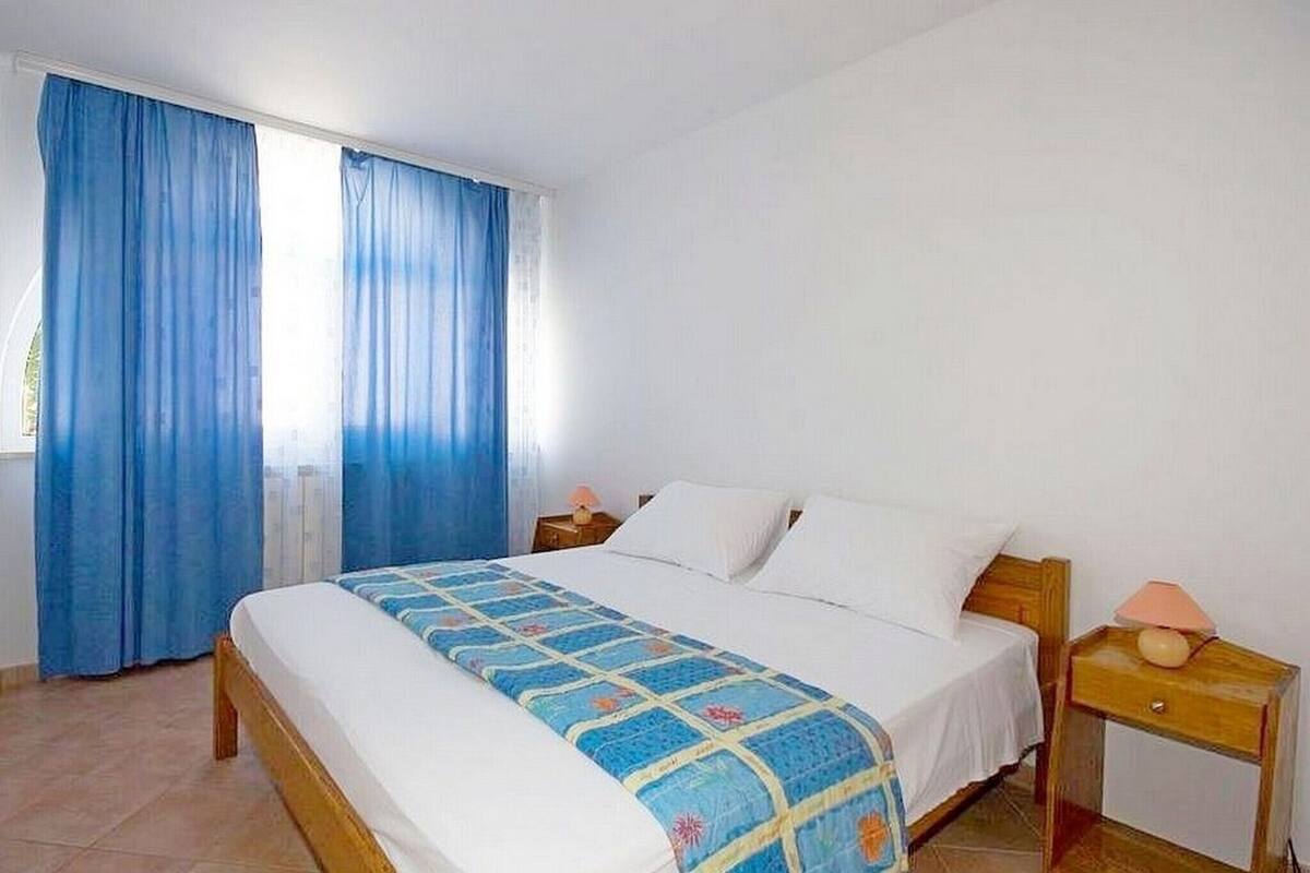 A bedroom with a bed, curtains, a nightstand, and a lamp.