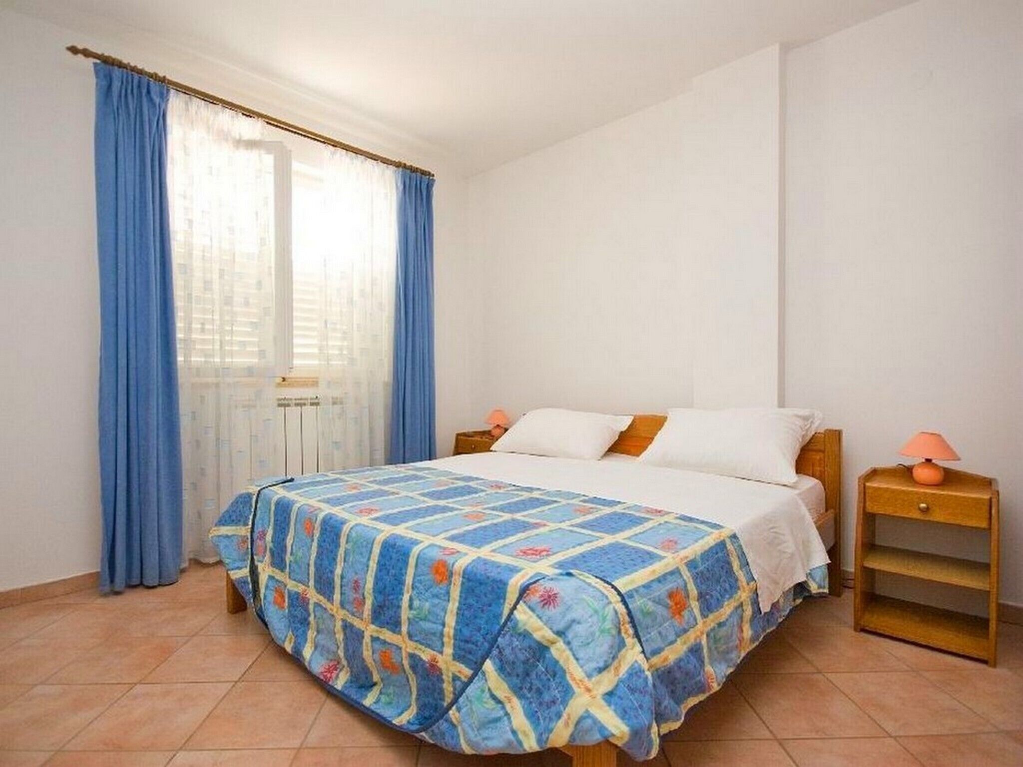Une chambre à coucher avec un lit, des rideaux, une table de chevet et une lampe.