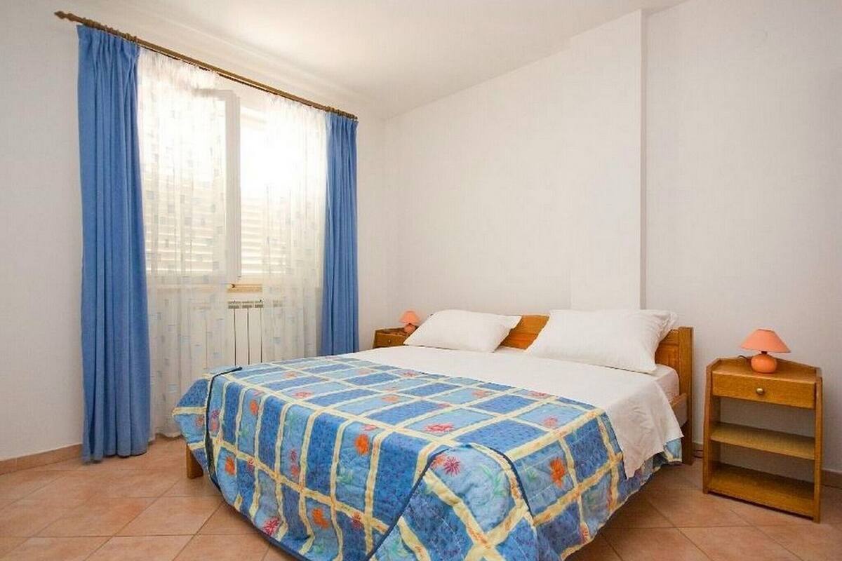 A bedroom with a bed, curtains, a nightstand, and a lamp.