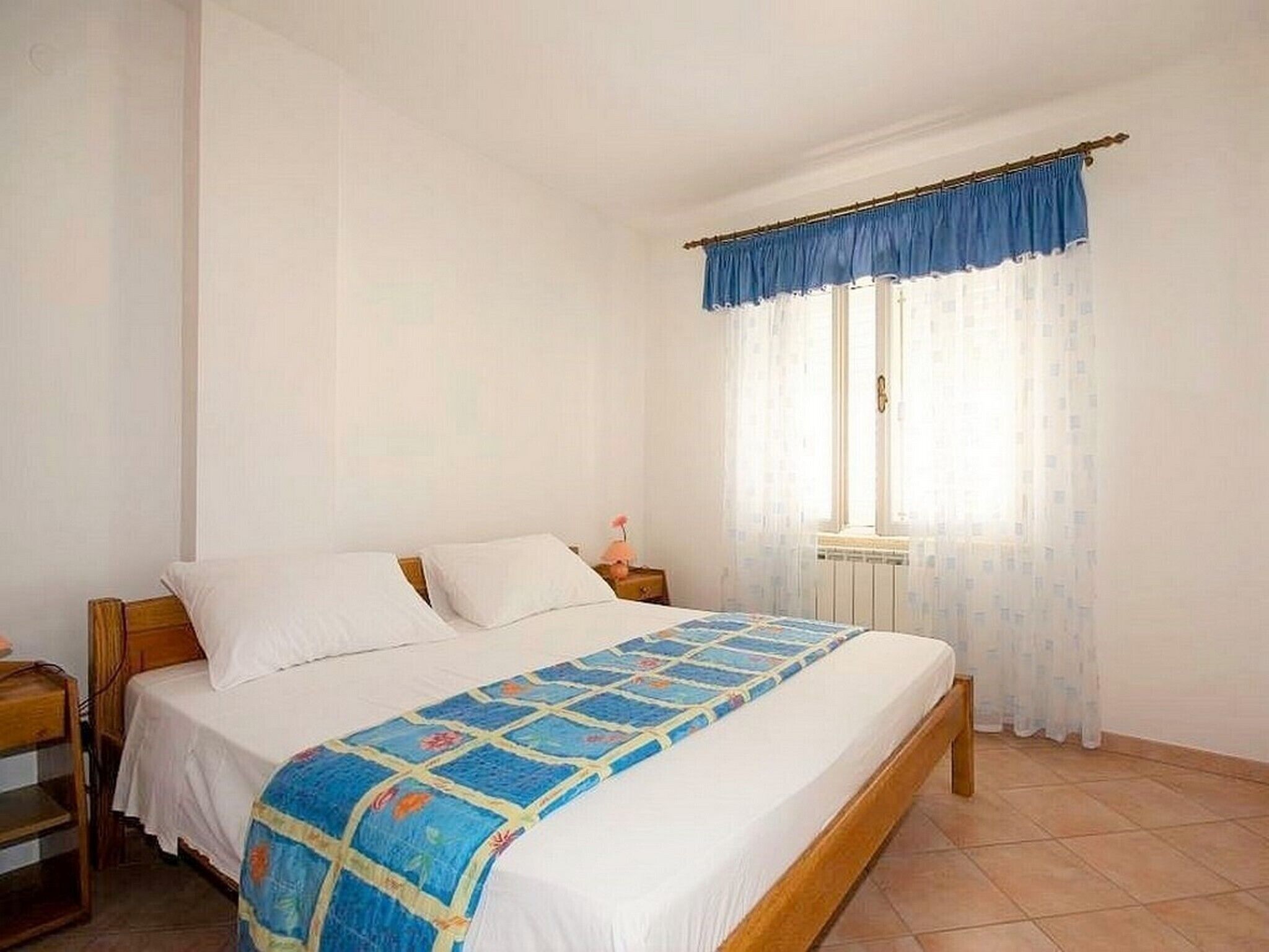 Une chambre à coucher avec un lit, une table de chevet, une fenêtre avec des rideaux et un radiateur.