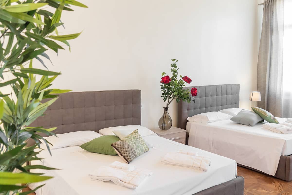 A hotel room with two beds, a vase with flowers, and a lamp.