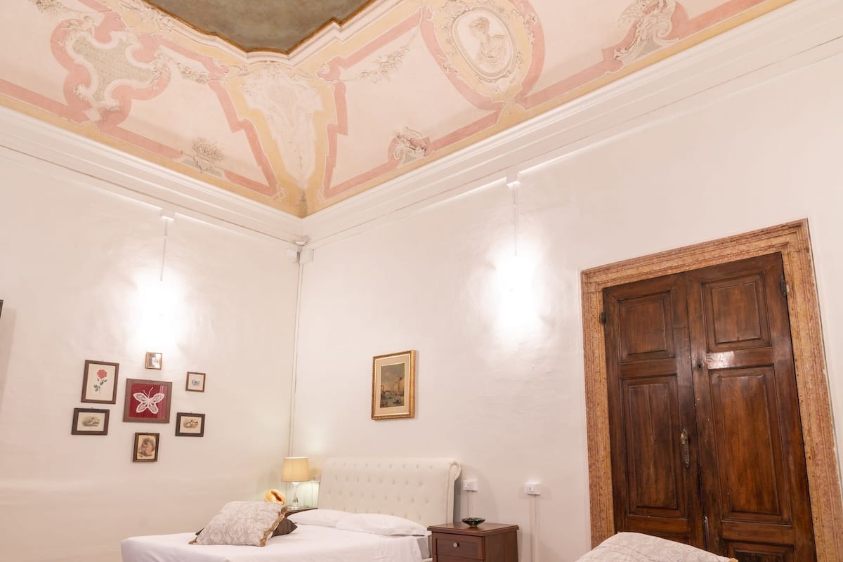 A room with two beds, a wooden wardrobe, and a ceiling mural.