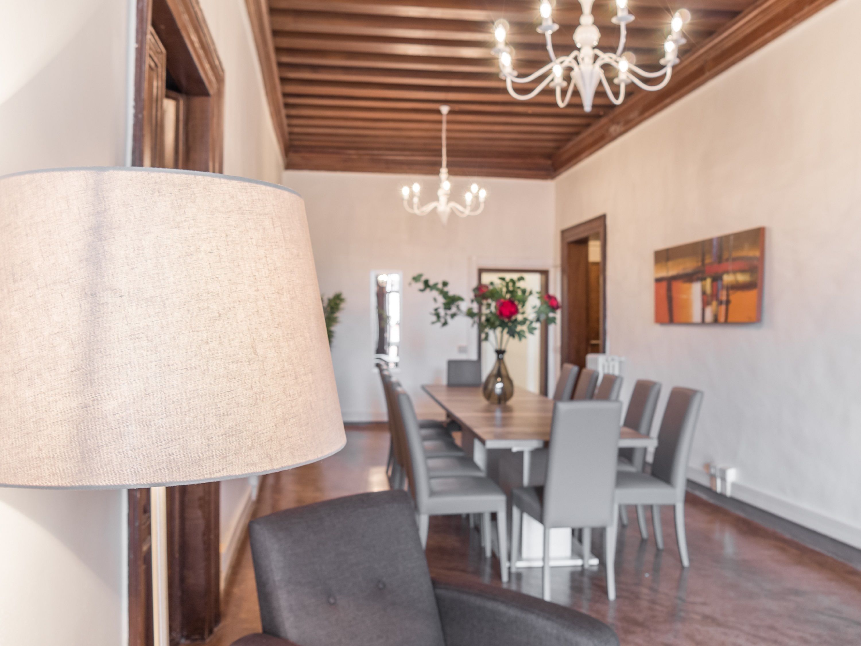 A dining area with a chandelier, a table with chairs, and a vase with flowers.