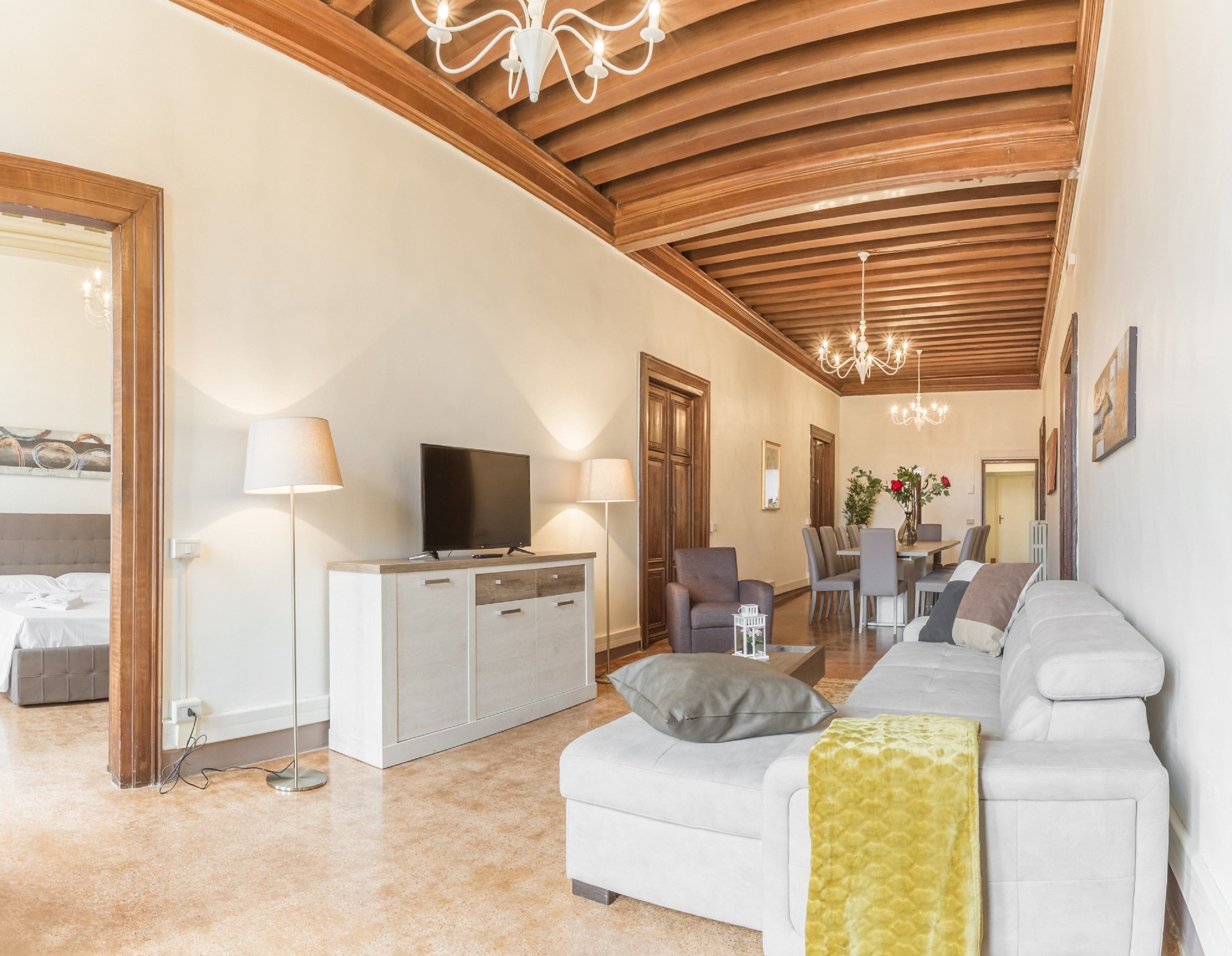 Uma sala de estar ampla com um sofá moderno, uma televisão sobre um móvel, e um espaço de jantar com cadeiras e uma mesa.