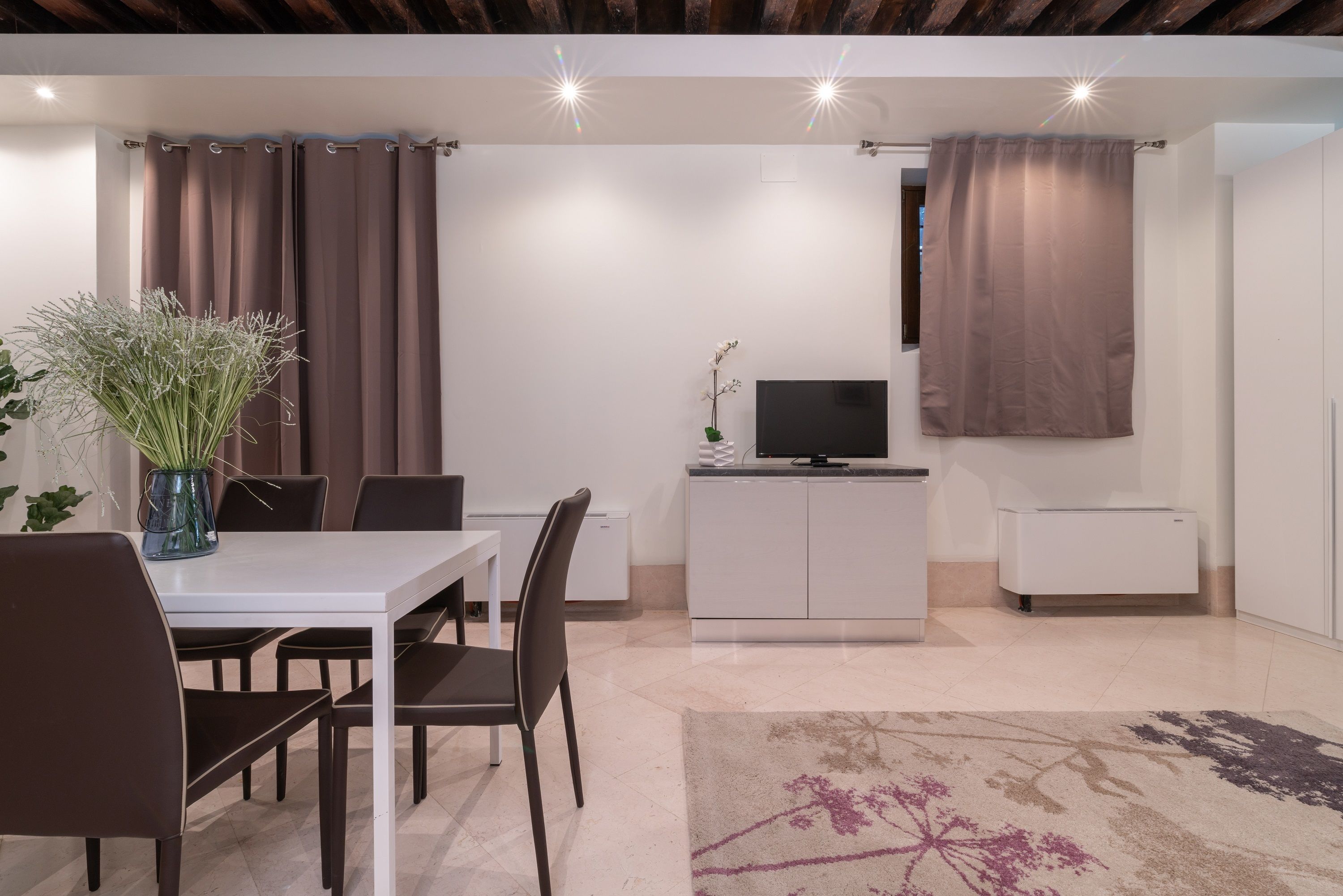 Un soggiorno moderno con zona pranzo, televisore piatto e mobiletto bianco.