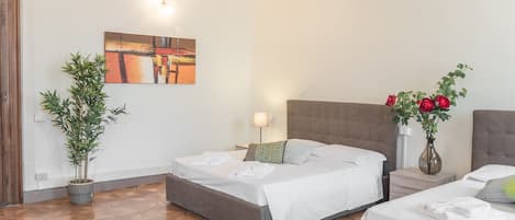 Una habitación de hotel con dos camas, un cuadro en la pared, una planta en maceta y un jarrón con flores.