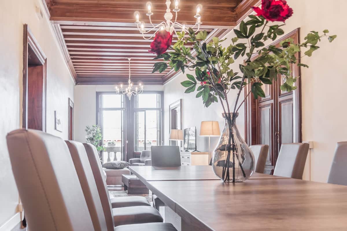 A dining area with a long wooden table, multiple chairs, a vase with flowers, and a chandelier.