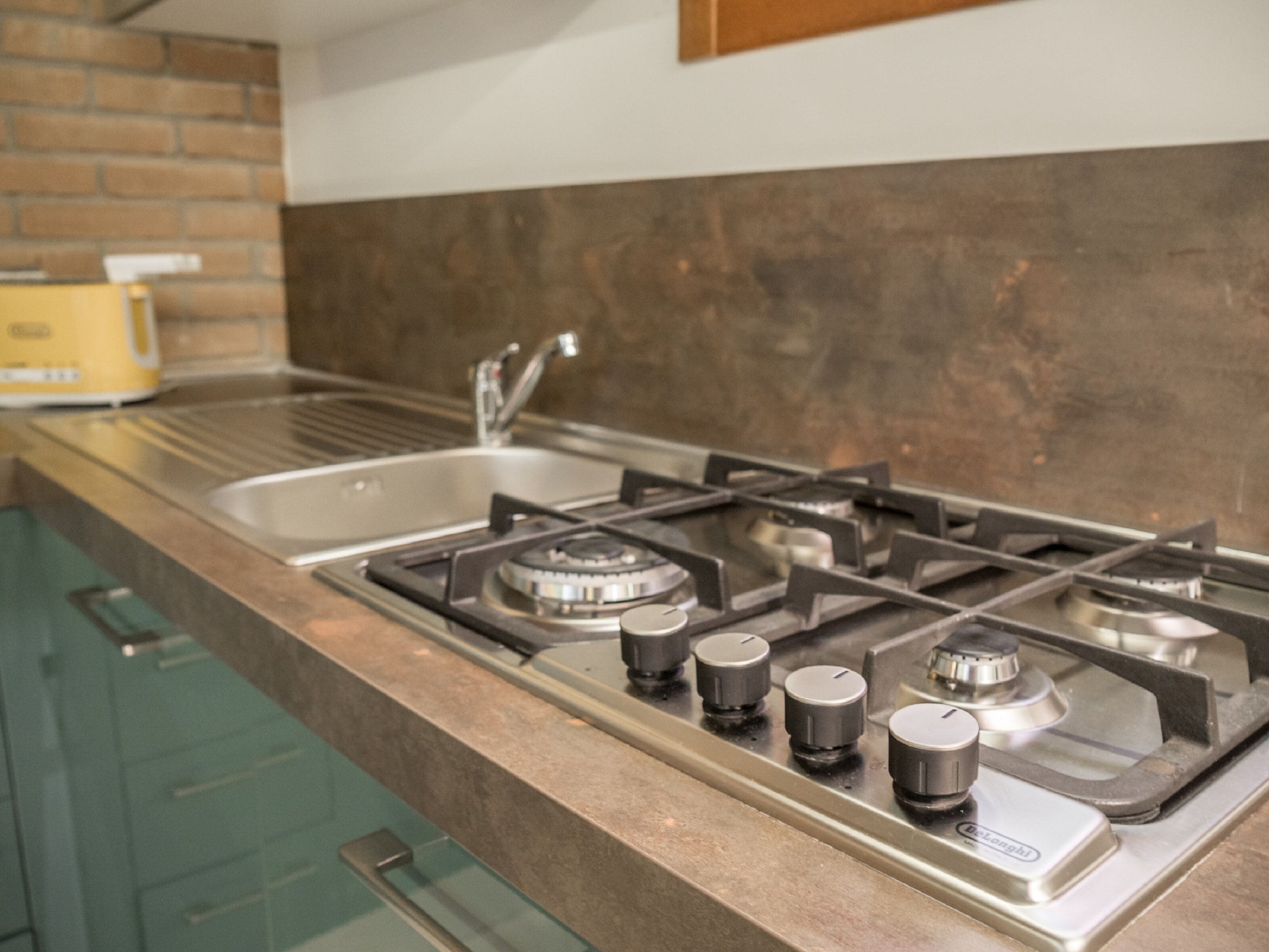 A kitchen with a gas stove, stainless steel sink, and a brick backsplash.