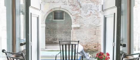 Un balcón con dos sillas de metal y una mesa, con vista a un patio de ladrillo y un arco.
